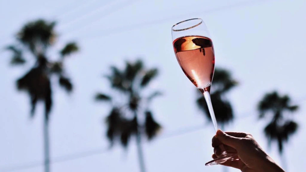 Hand holding a pink champagne flute in front of a skyline of silhouetted palm trees