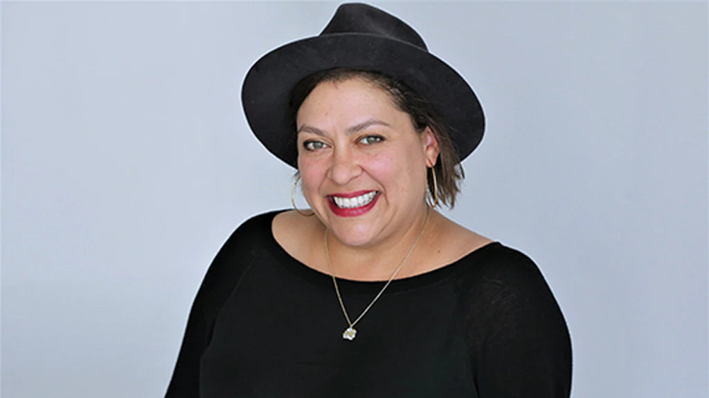 Portrait of Vinovore owner, Coly Den Haan in a studio, wearing a black hat, black top and a gold necklace