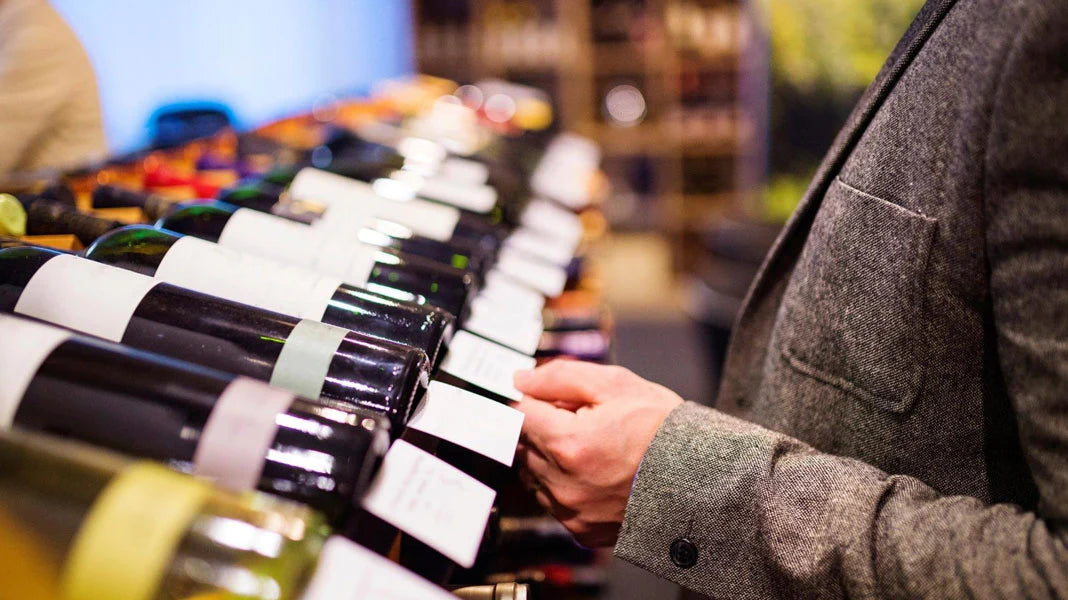 Photo of a person in a tweed jacket looking at a shelf of wine, reading the tag info