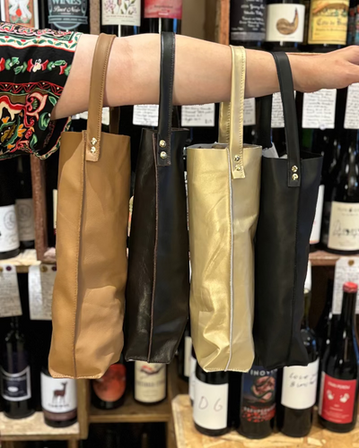 Four leather wine bottle holders displayed in front of a shelf of wine bottles.