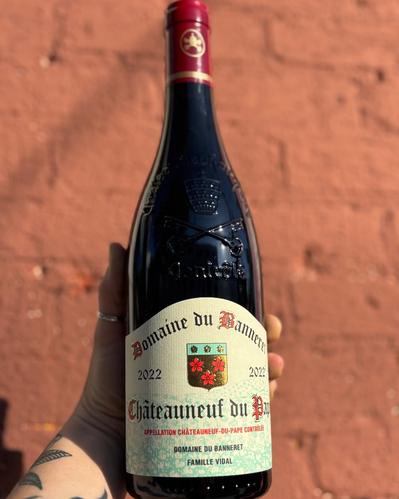 Bottle of Domaine du Banderet Chateauneuf-du-Pape wine held against a brick wall.