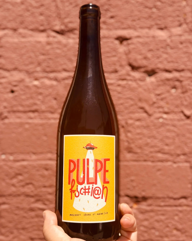 Bottle of Pulpe fashion with a yellow label held against a brick wall.