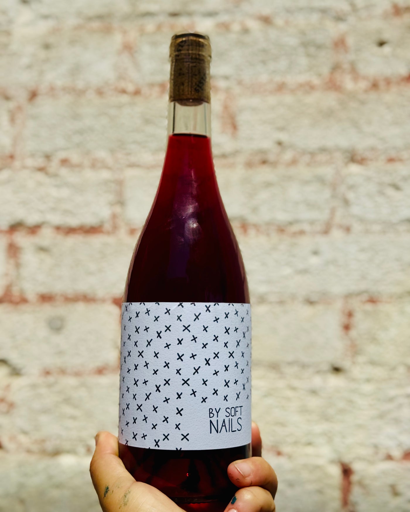 Bottle of red wine with a patterned label held against a textured wall.