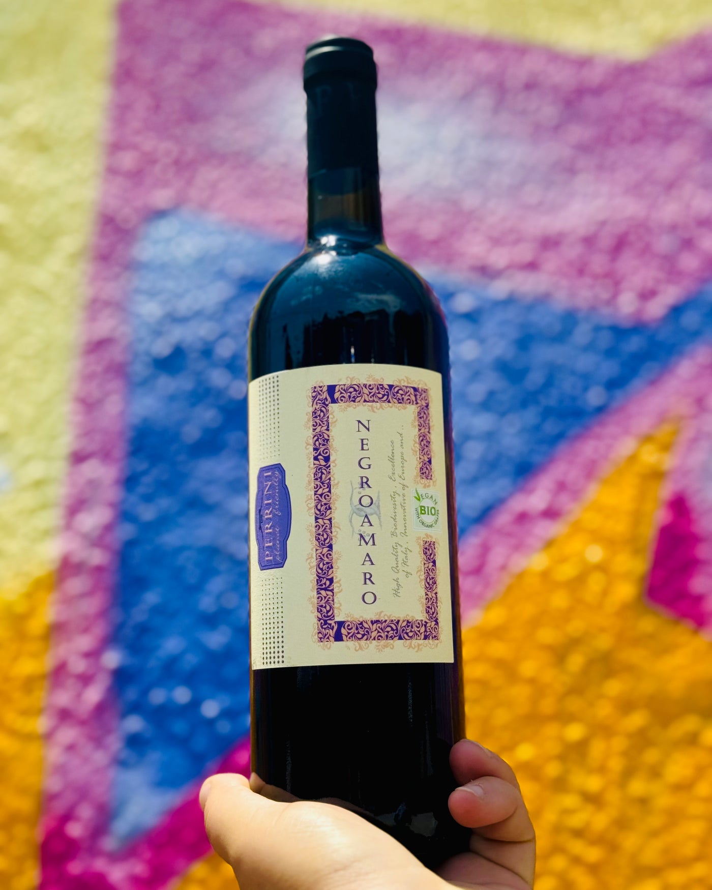 Bottle of Negramaro wine held against a colorful abstract background
