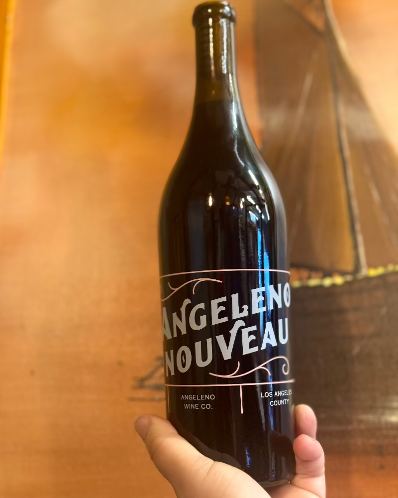 Bottle of Angeleno Nouveau wine held in front of a wooden background