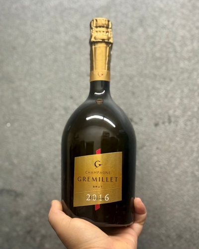 Bottle of Gremillet champagne held by a hand against a gray background