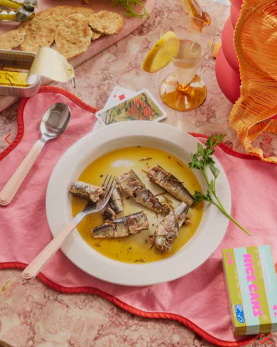 Dish of fish with a yellow sauce on a pink tablecloth with a teapot and snacks.