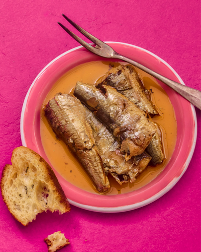 Pink plate with fried fish and bread on a pink background