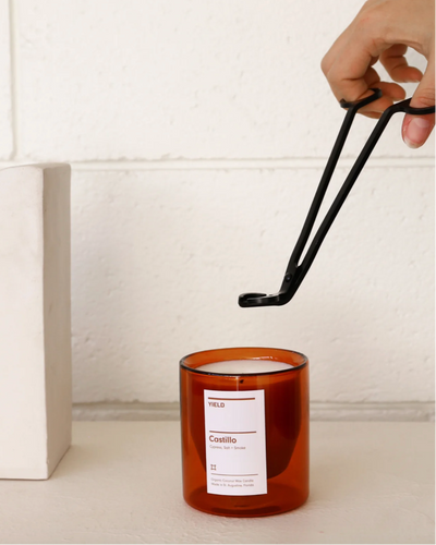 Candle with a label being held by tongs against a white background