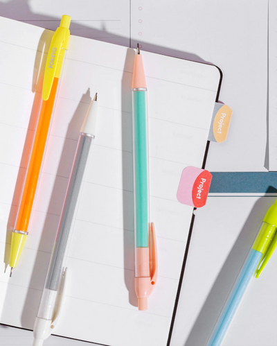 Colorful pens attached to a notebook with colorful flags on a white background