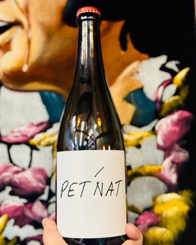 Bottle of Pet Nat held in front of a colorful floral background